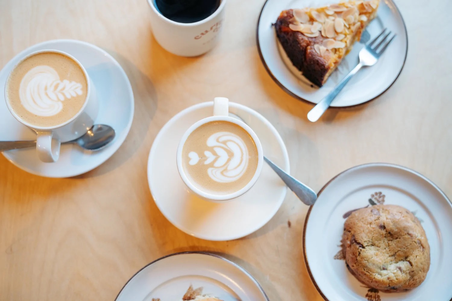 Flat whites, almond cake and a cookie on a table at Curve